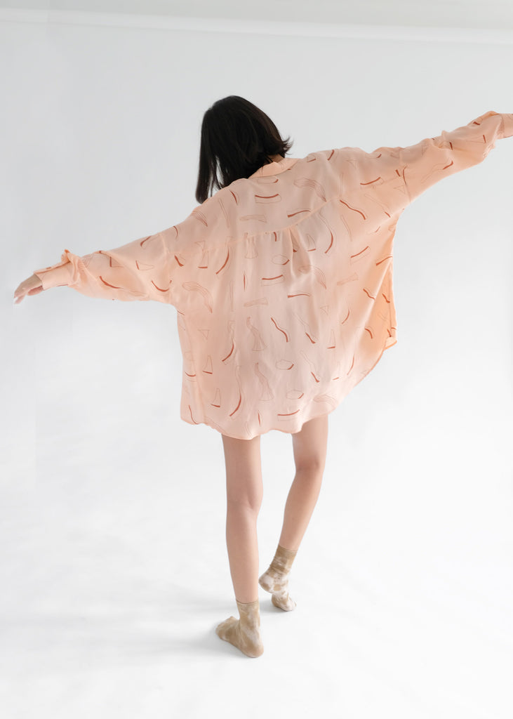Girl standing backwards wearing pink silk printed shirt 