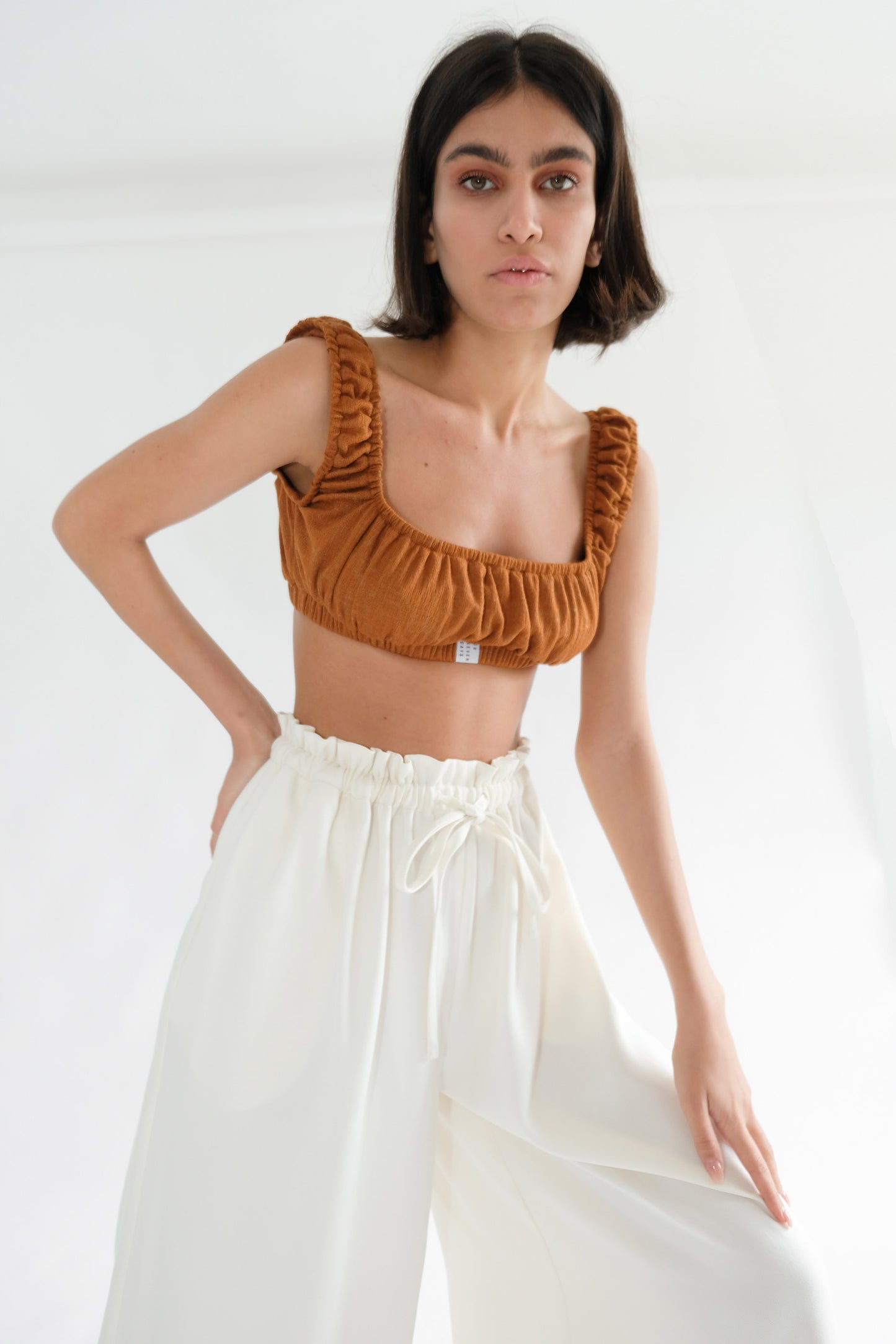 Girl standing wearing brown underwear set and white trousers