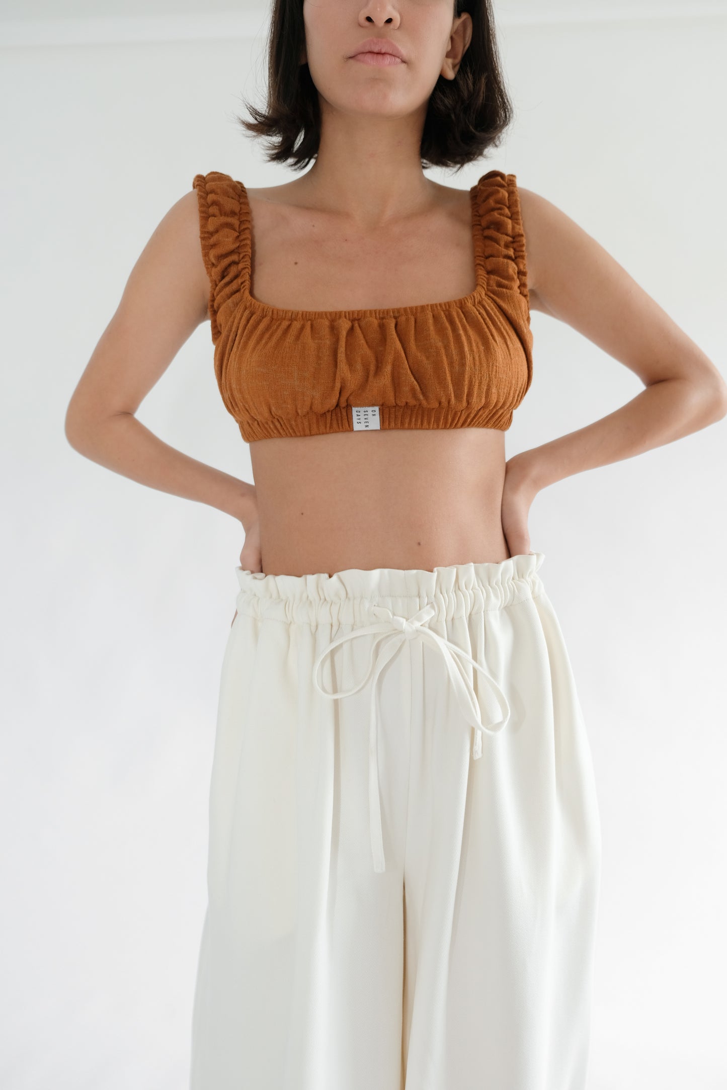 Girl standing wearing brown underwear set and white trousers