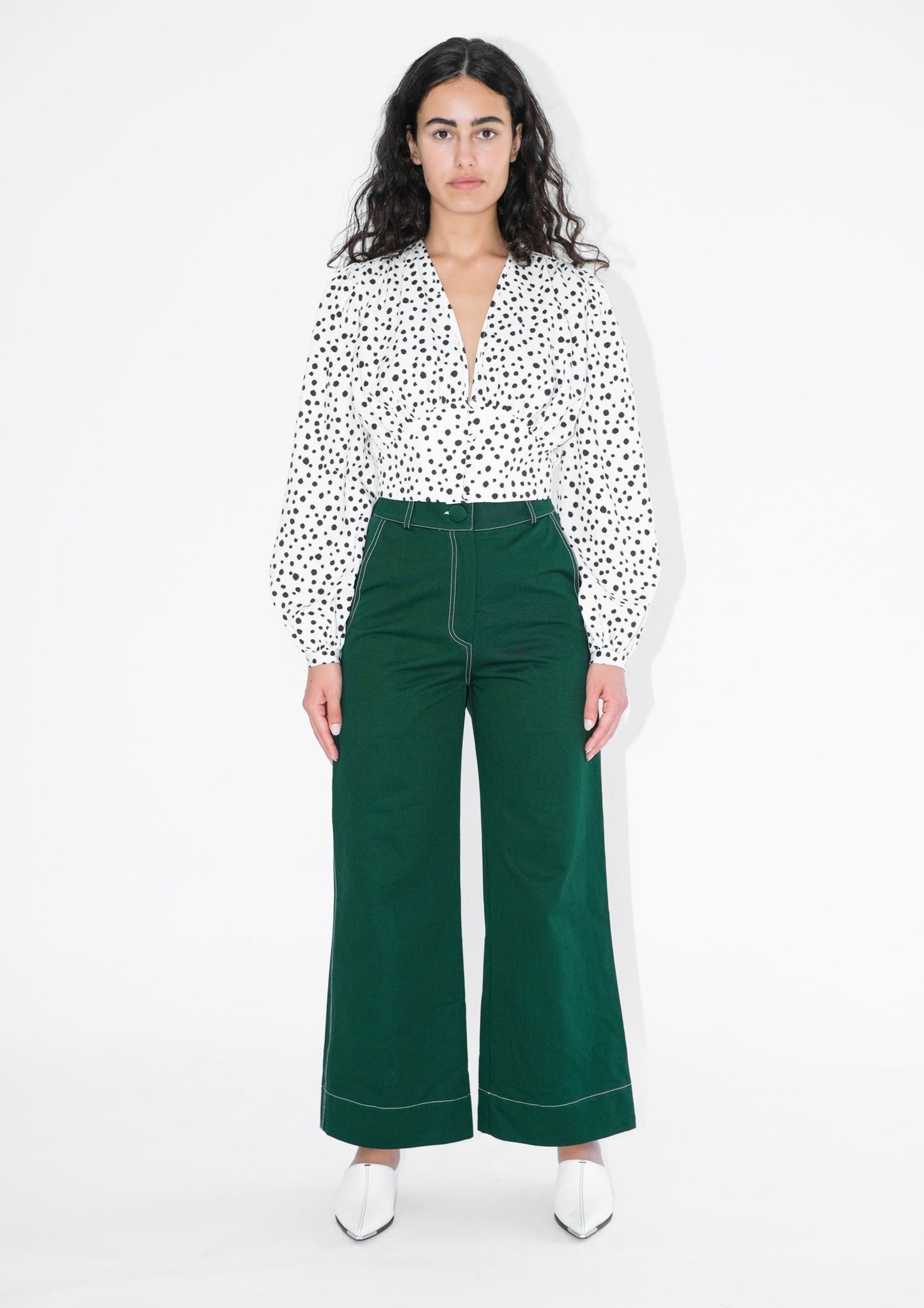 Woman wearing white shirt with black polka dots and green trousers