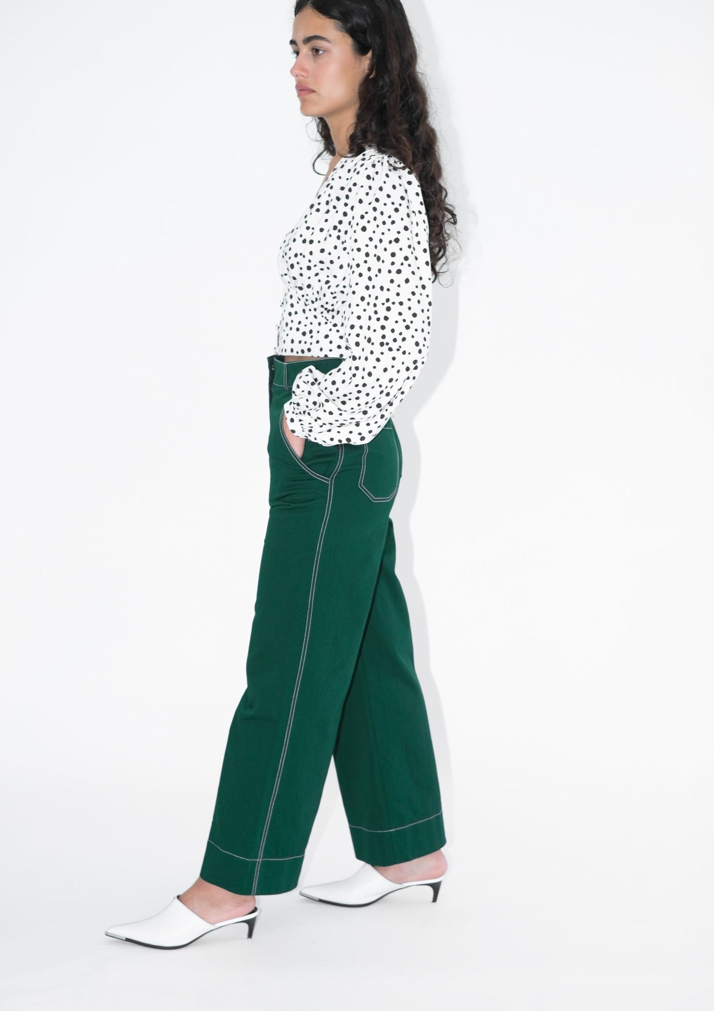 Woman wearing pine green trousers and white blouse with black polka dots