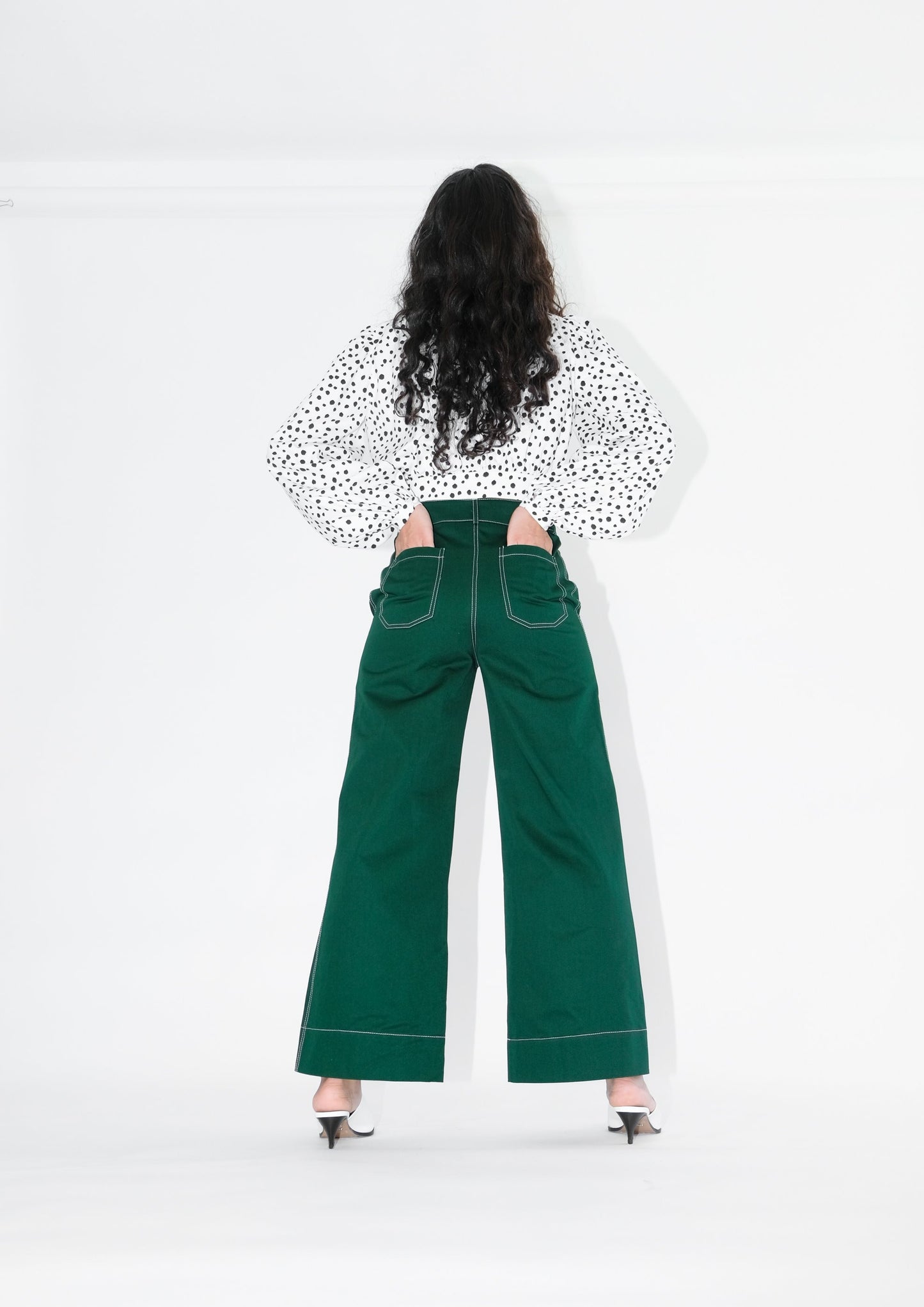 Back view of woman wearing pine green trousers and white blouse with black polka dots