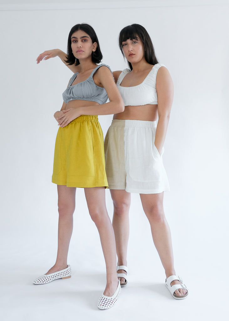 Two girls standing wearing blue and white tops with yellow shorts 