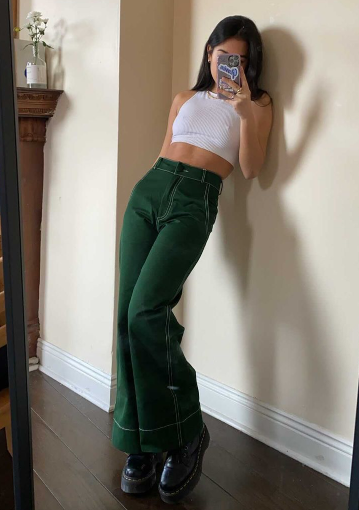 Woman taking mirror selfie wearing white tank top and pine green trousers
