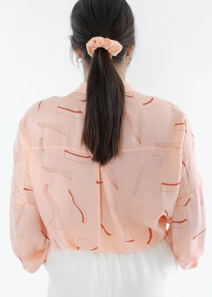 Girl standing backwards wearing pink silk printed shirt