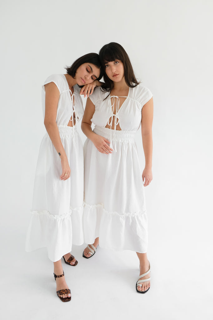 Two girls standing wearing white midi dresses 
