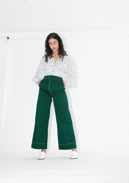 Woman wearing white blouse with black polka dots and pine green trousers