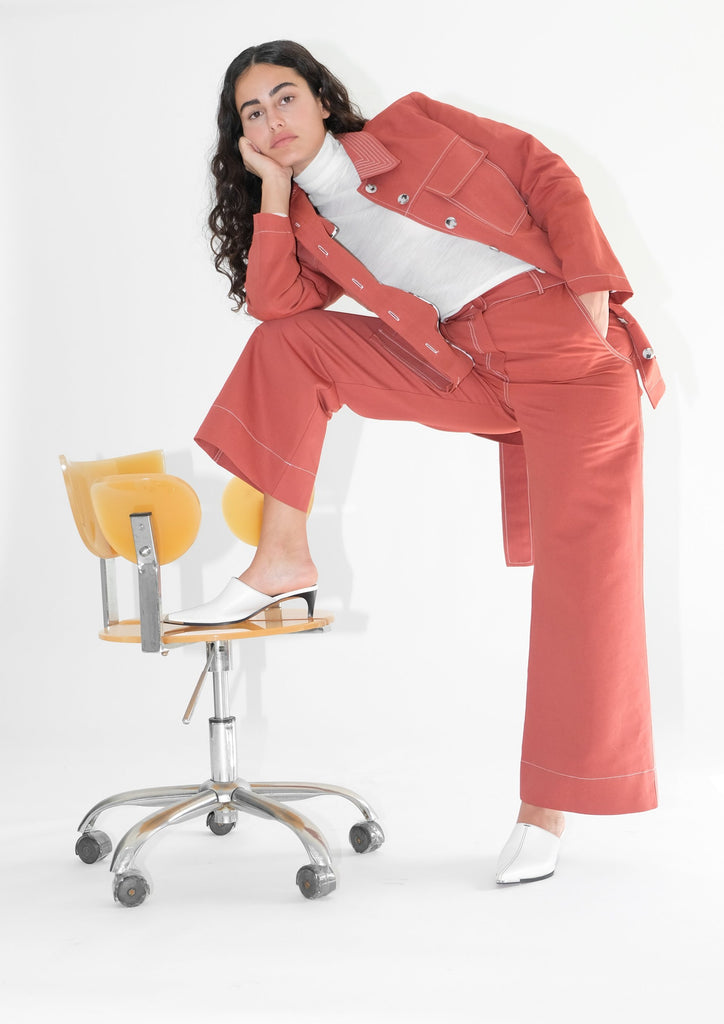 Woman wearing red trousers and red jacket with white turtleneck underneath next to a yellow chair