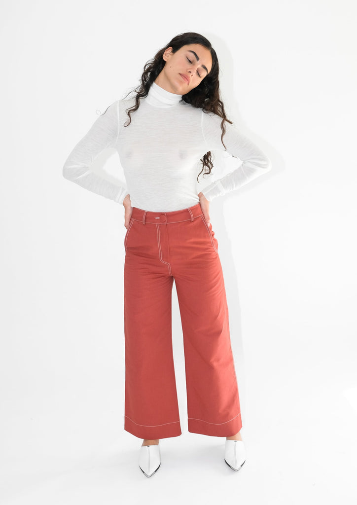 Standing woman wearing red flared trousers and white turtleneck