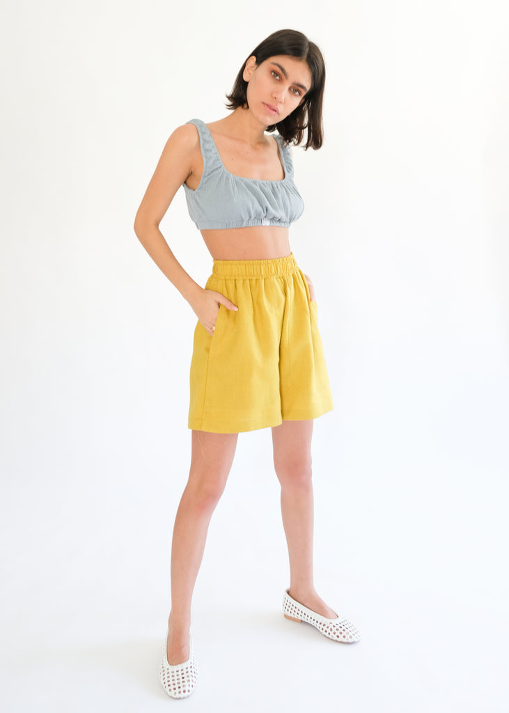 Girl standing wearing blue top and yellow shorts 